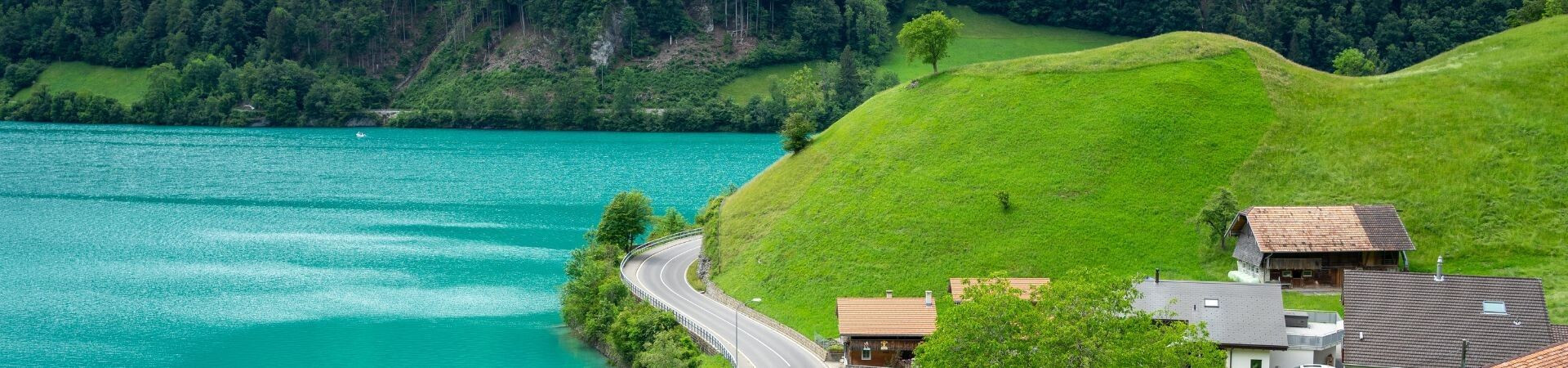 Route longeant un lac turquoise et collines verdoyantes - Suisse